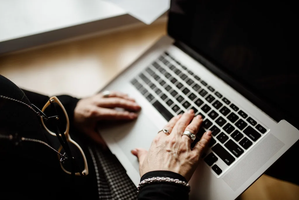 技术服务与办公场景：A middle-aged businesswoman typing on a laptop, wearing rings and bracelets, sitting in a well-lit workspace.